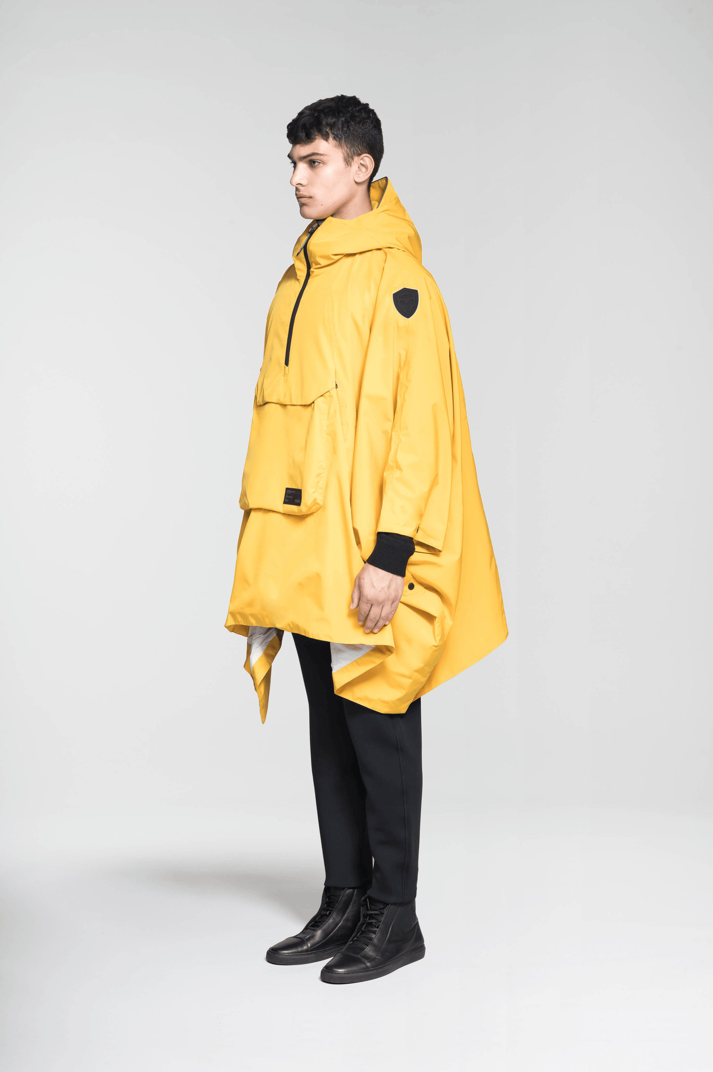 Hydra Unisex Performance Poncho in thigh length, non-removable hood, vertical half-zipper along centre front collar, hidden side-entry waist zipper pockets, adjustable webbing straps and snap closure cuffs, and packable to front kangaroo pocket with flap opening, in Old Gold
